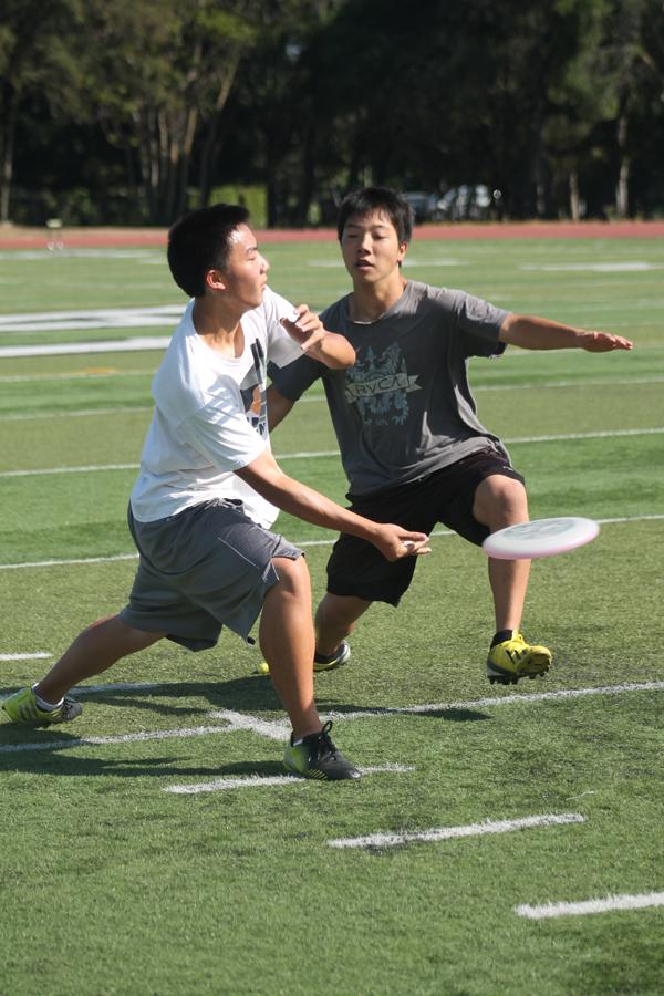Ghenki Okumoto straddles in at attempt to block Allen Zheng’s throw during an ultimate practice on the Paly football field. 