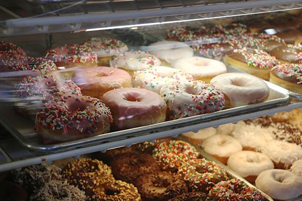 Dozens of doughnuts sit in rows in Happy Donuts display case, enticing customers with their sugary goodness