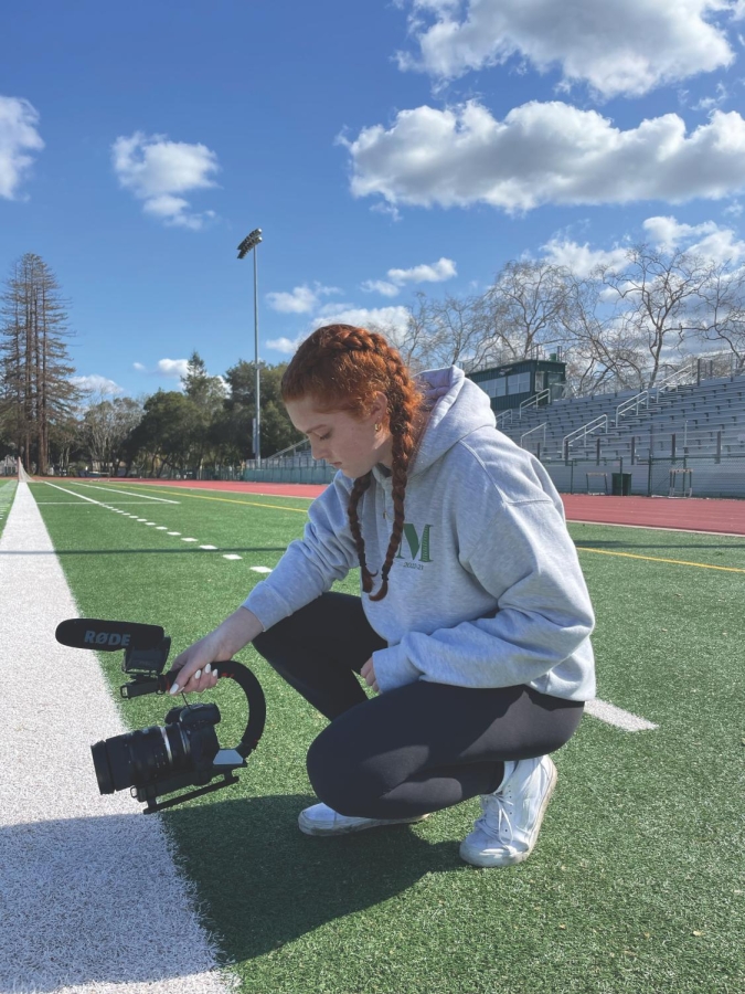 FIELD FILM —  Palo Alto High School junior Clare Antonow kneels by the sideline with her camera. “Football was definitely a hard one to start out with just because you really have to stand there for like two hours straight, ” Antonow said. “And that’s not even including pregame, postgame and sideline stuff.” Photo: Tate Hardy  