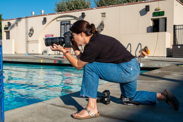 PICTURE PERFECT — Celeste Bates kneels down, focused on capturing a water polo match. “As a spectator, you’re [just] watching the plays,” Bates said. “[But] when you’re shooting it, you want to be able to tell the story to someone who wasn’t there.” 